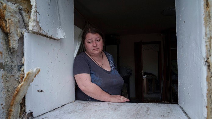 Žena sa pozerá cez okno svojho poškodeného domu po ruskom nálete na obytnú štvrť v Charkove.