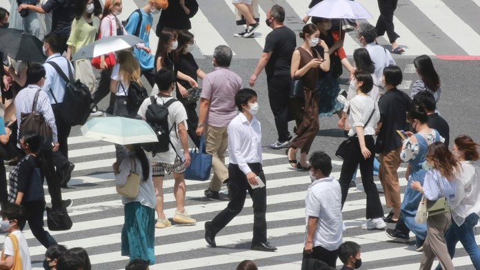 Ľudia s ochrannými rúškami kráčajú po priechode pre chodcov v Tokiu.