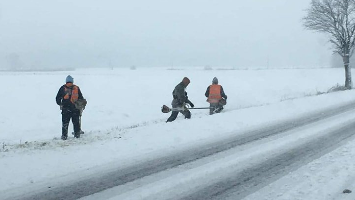 Cestári kosia zasneženú trávu.