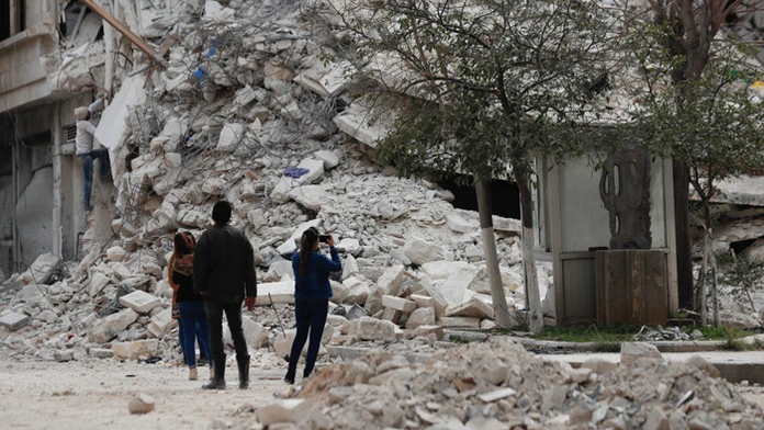 Ľudia stoja pri budove, ktorá sa zrútila v dôsledku nedávneho zemetrasenia v sýrskom meste Aleppo.