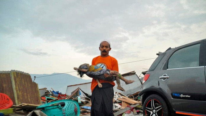 Muž vynáša detské telo spod trosiek domu, ktorý zničila vlna cunami.