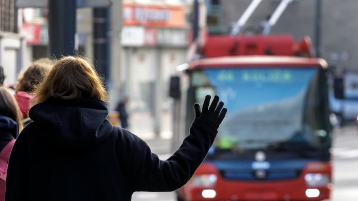 Na snímke žena máva na zastávke na červený autobus MHD, ktorý sa k nej blíži.