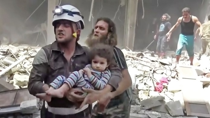 Na snímke miestny člen civilnej obrany  Biele helmy nesie dieťa po náletoch v povstalcami ovládanej časti mesta Aleppo 