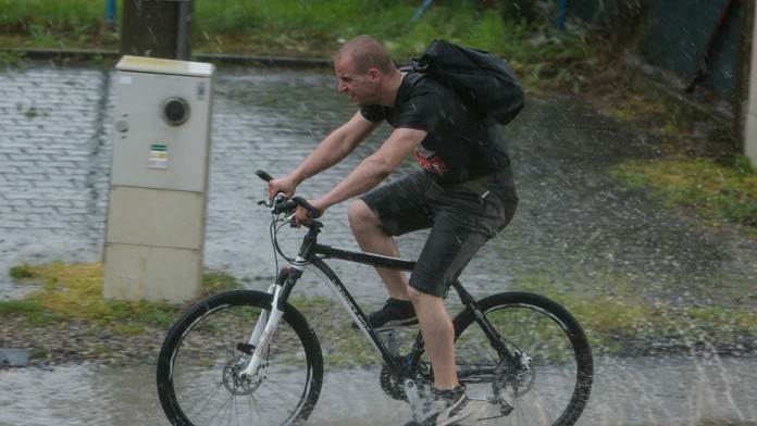Cyklista jazdí po ceste, kde voda nestíha odtekať v dôsledku silnej búrky v Bratislave.