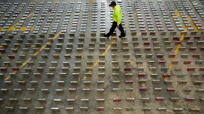 Policajt prechádza medzi zoradenými balíčkami kokaínu.