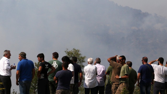 Ľudia sledujú vrtuľník počas hasenia lesného požiaru v oblasti juhozápadne od Nikózie.