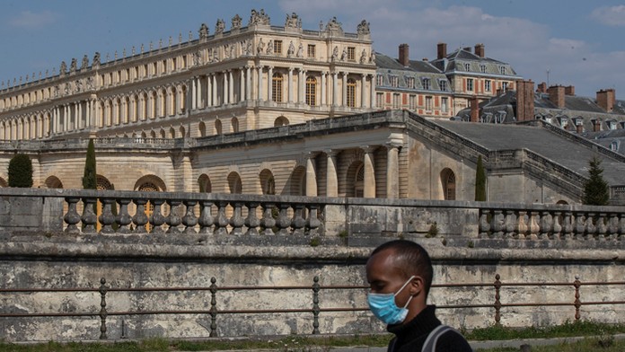 Muž s ochranným rúškom kráča vedľa zámku Versailles.