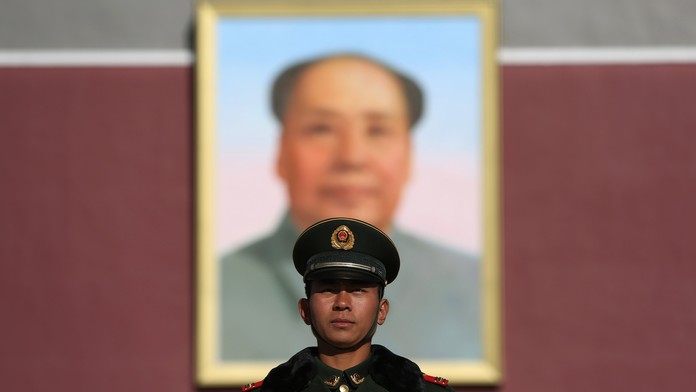 Čínsky policajt stojí pred vchodom do Zakázaného mesta s nadrozmerným obrazom Mao Cetunga v Pekingu.