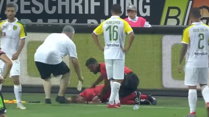 Rozhodca leží na trávniku po zásahu fľašou.