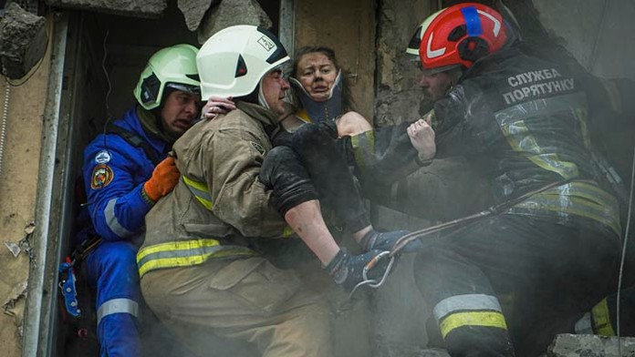 Ukrajinskí hasiči nesú zranenú ženu z ruín obytnej budovy v ukrajinskom meste Dnipro.