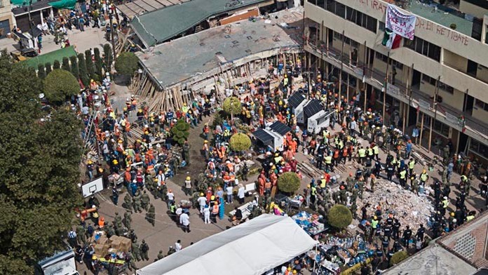 Dobrovoľníci a  záchranári  pátrajú po preživších deťoch v troskách zrútenej  školy. 