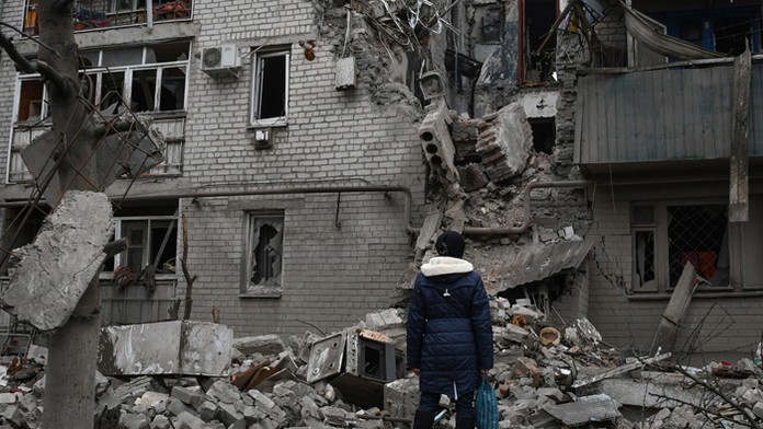 Žena sa pozerá na bytovku zničenú po nedávnom ruskom raketovom útoku v meste Časiv Jar v Doneckej oblasti.