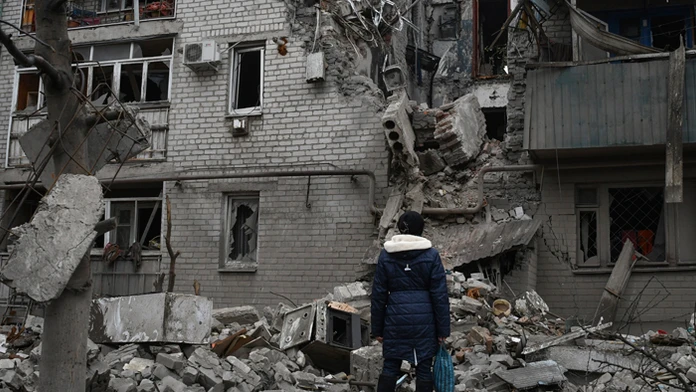 Žena sa pozerá na bytovku zničenú po nedávnom ruskom raketovom útoku v meste Časiv Jar v Doneckej oblasti.