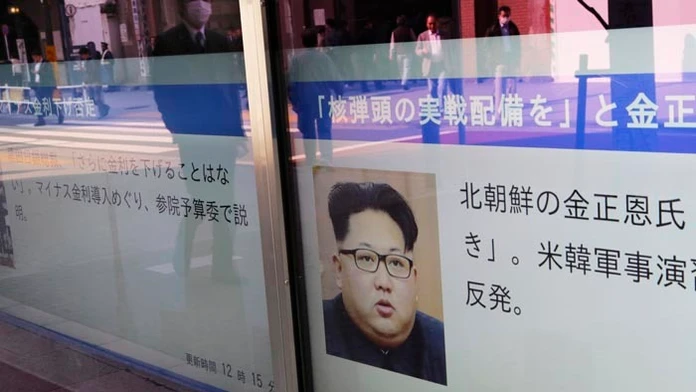 Ľudia v odraze výkladu kráčajú okolo portrétu severokórejského lídra Kim Čong-una v Tokiu.