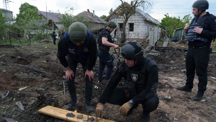 Ukrajinský policajt a prokurátor pre vojnové zločiny si prezerajú úlomky bomby pred poškodeným domom po ruskom ostreľovaní obytných častí mesta Charkov.