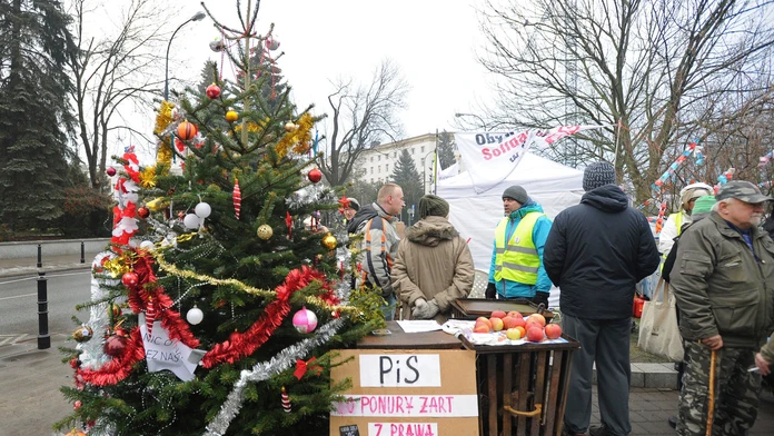 Poľskí opoziční poslanci stoja počas protestu pred budovou parlamentom. Skupina sa na protest proti opatreniam zavádzaným vládnu