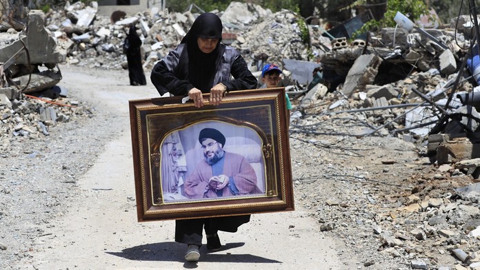 Žena nesúca portrét vodcu Hizballáhu po zbombardovanej ulici