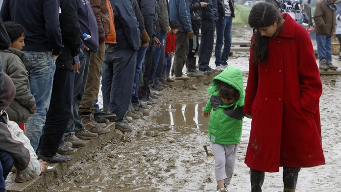 Migrantka kráča s dieťaťom cez blato v utečeneckom tábore pri severogréckej dedine Idomeni na macedónsko-gréckej hranici.