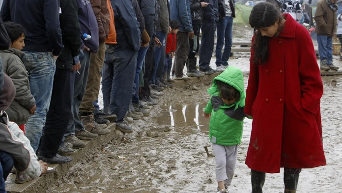 Migrantka kráča s dieťaťom cez blato v utečeneckom tábore pri severogréckej dedine Idomeni na macedónsko-gréckej hranici.