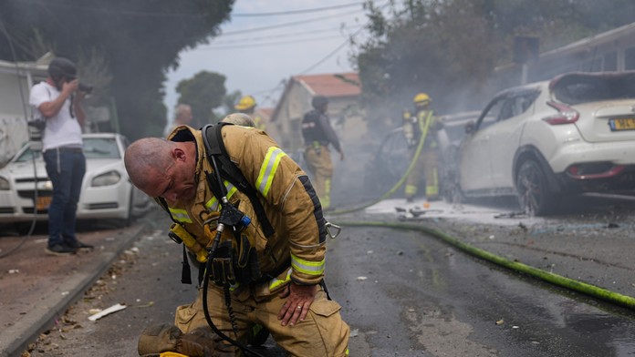 Izraelský hasič reaguje na kolenách po hasení horiacich áut zasiahnutých raketami vystrelenými z pásma Gazy v izraelskom meste Aškelon.