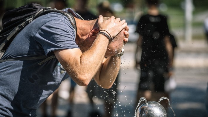 Muž si v horúčave chladí hlavu pri fontáne.