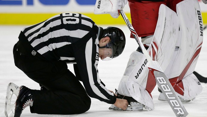 Čiarový rozhodca vyberá puk z korčule gólmana Caroliny Cama Warda.