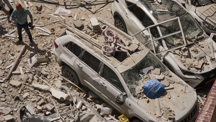 Na snímke muž sa pozerá na vraky áut a poškodenú obytnú budovou, ktorú zasiahla iránska raketa v izraelskom meste Ramat Gan.