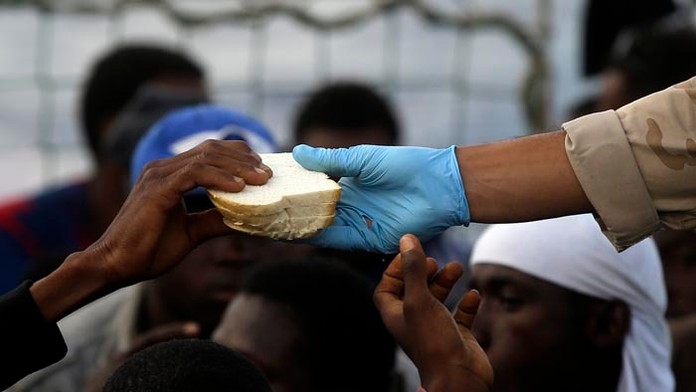 Belgický vojak ponúka zachráneným africkým migrantom kusy chleba na palube belgického námorného plavidla Godetia počas záchranne