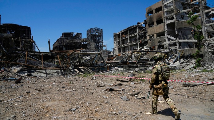 Ruský vojak kráča pred poškodeným závodom Azovstal v Mariupole.