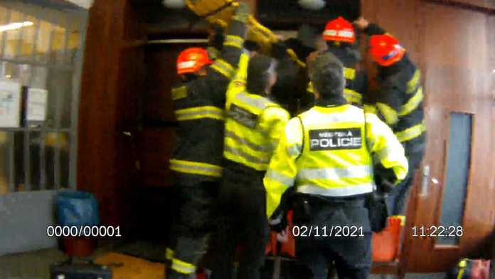 Hasiči s policajtmi sa snažia vyslobodiť seniorku zakliesnenú medzi stenou a výťahom.