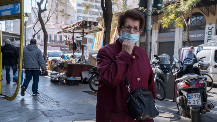 Staršia žena s ochranným rúškom kráča po ulici v Aténach.
