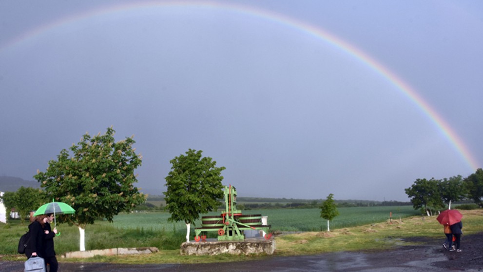 Ľudia v daždi prechádzajú pred dúhov v obci Čerhov.