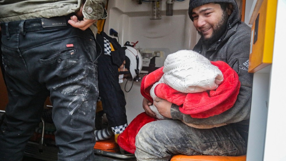 Muž drží v náručí dieťa po zemetrasení v sýrskom Aleppe.