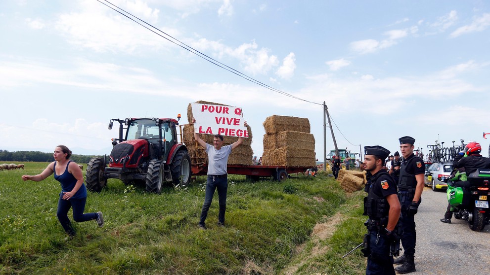 Policajti sledujú protestujúcich farmárov počas 16. etapy Tour de France.
