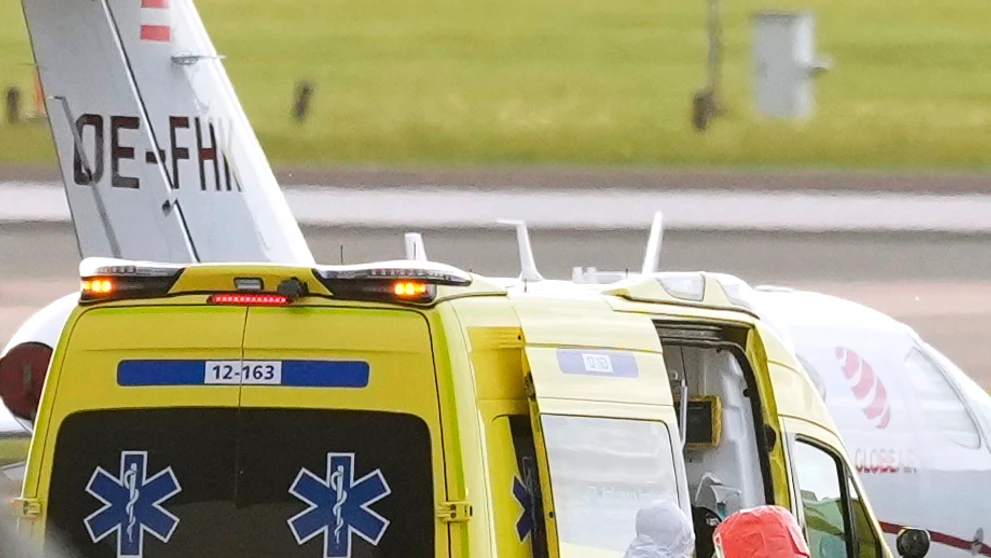 Zdravotný personál v špeciálnych ochranných odevoch pomáhajú pacientovi (druhý sprava) s podozrením na infekciu hantavírusom nasadnúť si do sanitky na letisku Schiphol v Amsterdame.