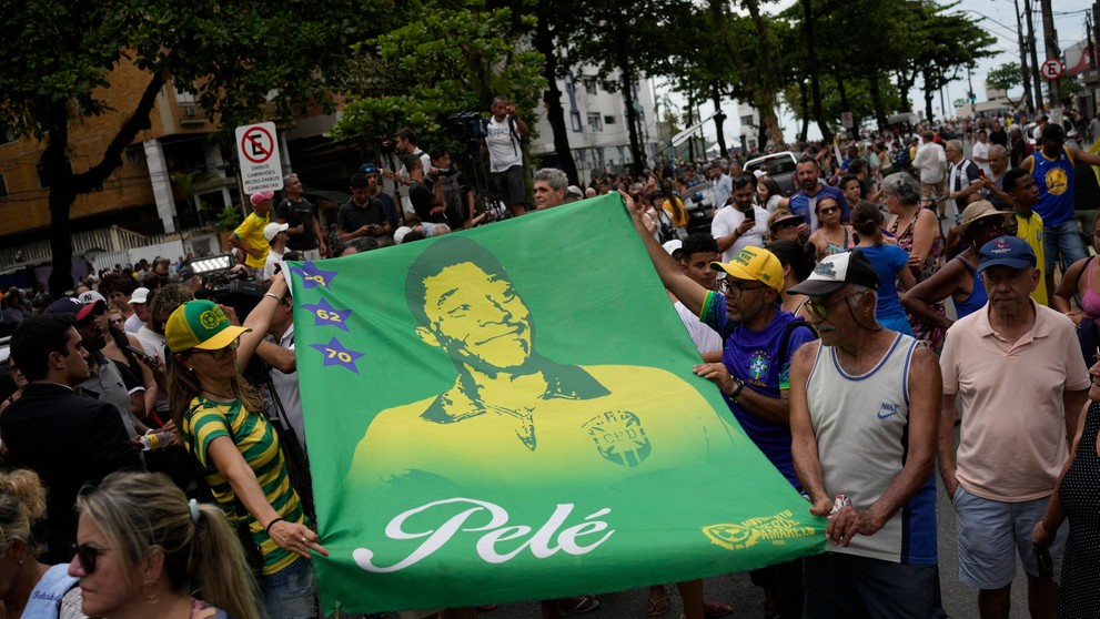 Ľudia držia transparent s podobizňou Pelého, zatiaľ čo rakvu s jeho telom prevážajú na cintorín.