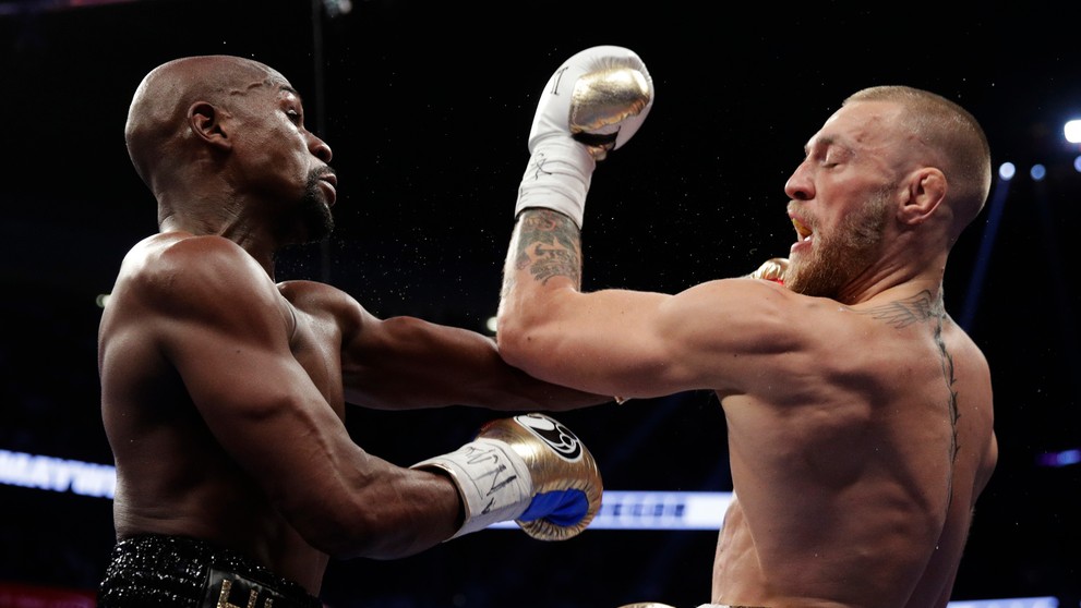 McGregor (vpravo) inkasuje úder od Mayweathera.