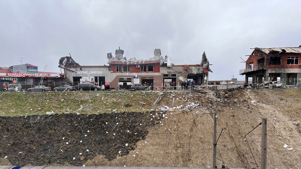 Prechádzajúci vlak, v pozadí záchranári odstraňujú následky útoku v Ľvove.