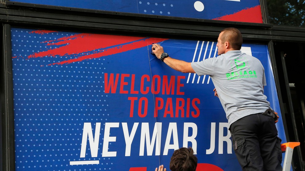 Zamestnanec pripevňuje uvítací transparent pre Brazílčana Neymara pred oficiálnym klubovým obchodom Paríža Saint-Germain.