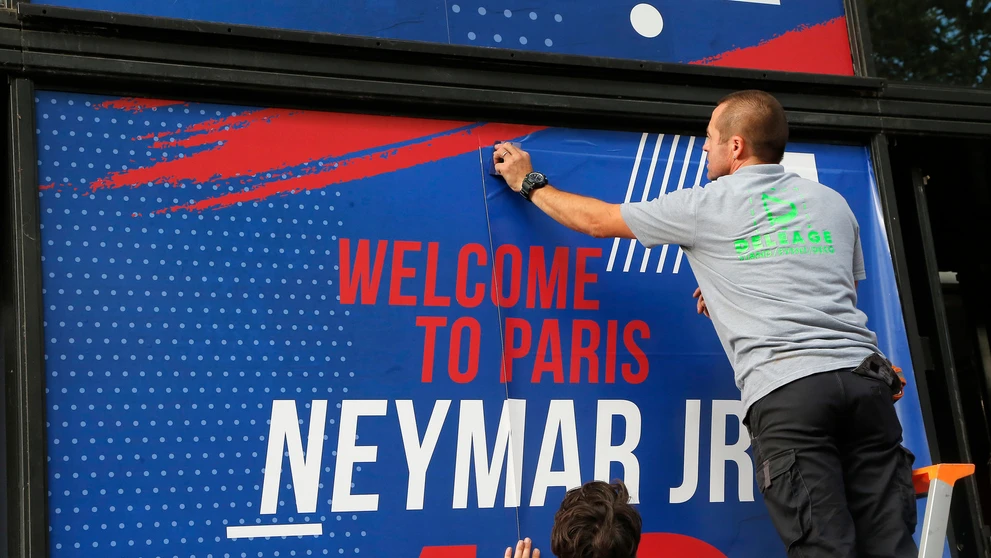 Zamestnanec pripevňuje uvítací transparent pre Brazílčana Neymara pred oficiálnym klubovým obchodom Paríža Saint-Germain.