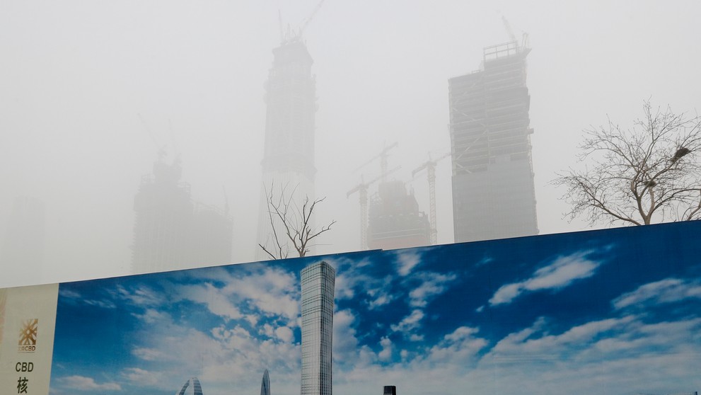 Do smogu zahalená obloha nad Pekingom v kontraste s panorámou na bilborde.