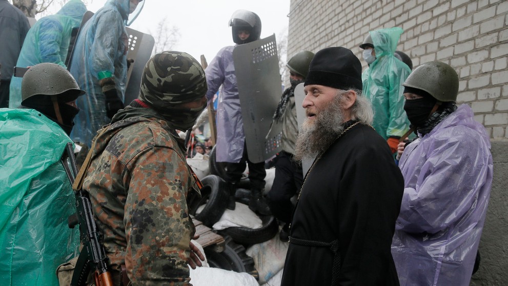 Pravoslávny kňaz sa rozpráva s proruským ozbrojeným strelcom pred obsadenou policajnou stanicou v ukrajinskom meste Slovjansk.