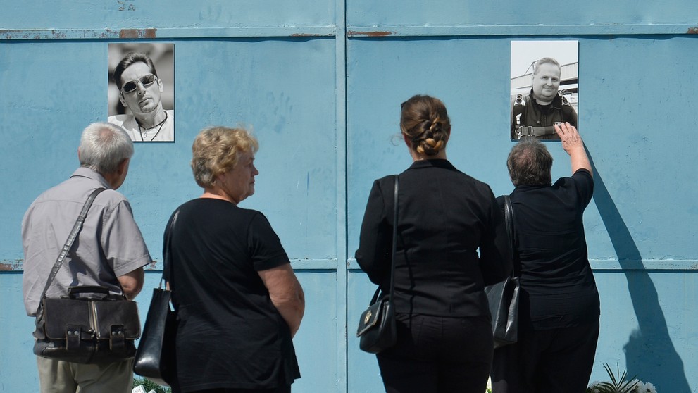 Pozostalí prinášajú kvety k fotografiám obetí leteckého nešťastia na bráne hangára