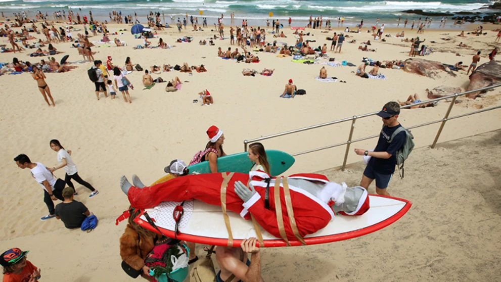 Figurína Santa Clausa je pripevnená na surfe, aby ju ľahšie prepravili po pláži Bondi Beach v Austrálii.
