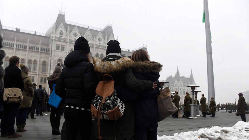 Ľudia sledujú spúšťanie štátnej vlajky na pol žrde.