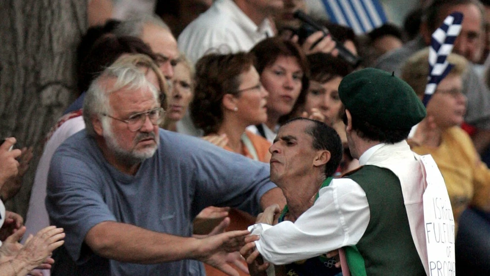 Neznámy muž v kostýme napadá favorita pretekov, brazílskeho atléta Vanderleia De Limu, na maratónskej trati v Aténach.