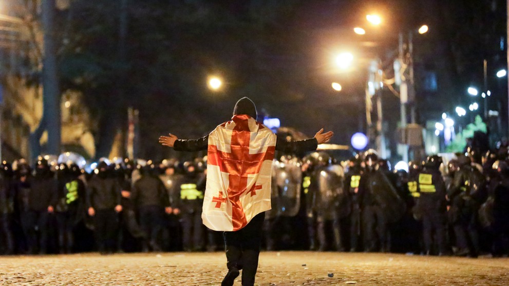 Demonštrant s gruzínskou vlajkou kráča k policajtom počas protestu pred budovou parlamentu v Tbilisi.