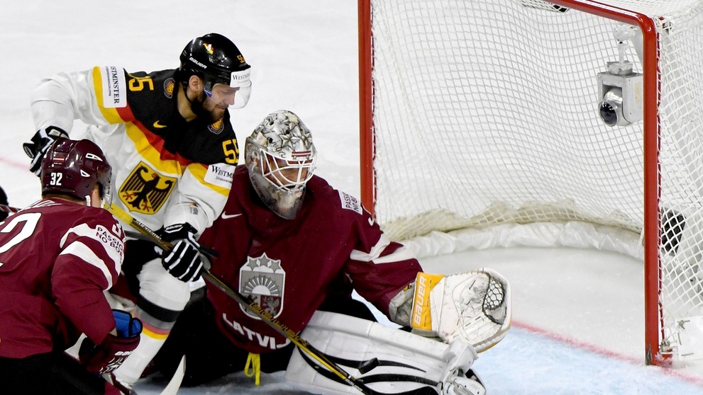 Felix Schütz (vľavo) z Nemecka útočí v dueli MS 2017 na lotyšského gólmana Elvisa Mezlikinša.