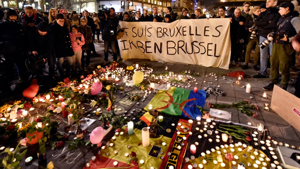 Na snímke ľudia držia transparent vedľa kvetov a sviečok na pamiatku obetí teroristických útokov v centre belgickej metropoly.