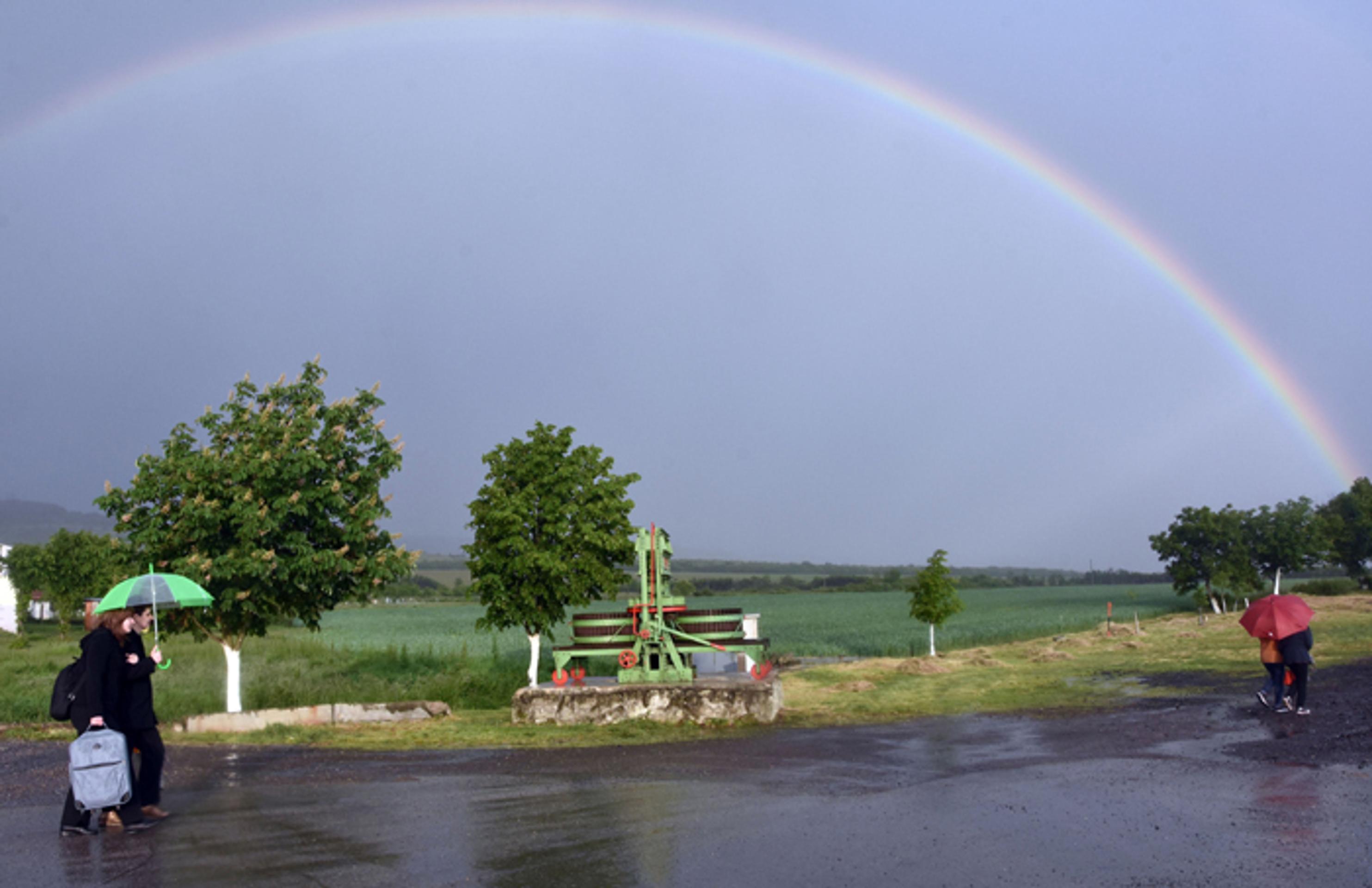 Ľudia v daždi prechádzajú pred dúhov v obci Čerhov.